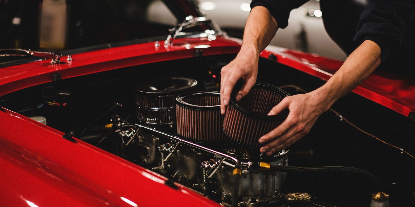 Mãos encaixando um filtro de ar novo no compartimento do motor de um carro vermelho